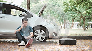 Asian man sitting beside car and using mobile phone calling for assistance after a car breakdown on street. Concept of vehicle