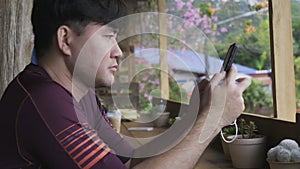 Asian man sitting in a coffee shop reading a message on a mobile phone. Handsome man using smartphone in the cafe.