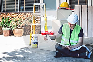 Asian man sitting on the floor,  working and looking a blueprint to plan renovate home