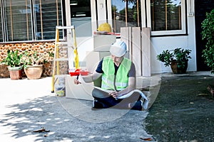 Asian man sitting on the floor, working and looking a blueprint to plan renovate home