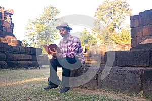 Asian man sitting and reading book in old stone temple.
