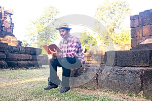 Asian man sitting and reading book in old stone temple.