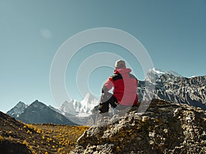 Asian man sitting on top of rock looking at view with Mount Yangmaiyong or Jampayang in Tibetan in the distance in Yading, China