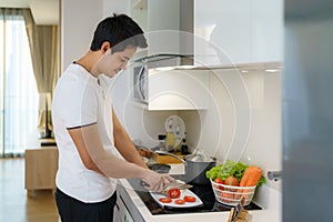 An Asian man slices tomatoes on a kitchen counter to prepare for dinner at home