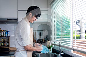 Asian man smile and washing a dish in kitchen room