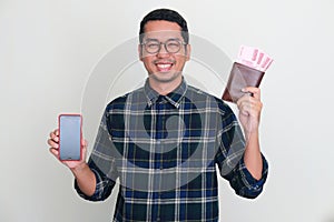 Asian man smiling confident while showing blank handphone screen and wallet full of money