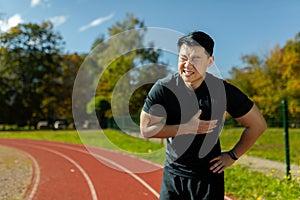 Asian man in sports training has severe heart pain, athlete with heart attack attack in stadium holding hand to chest