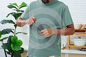 Asian man is standing grinding coffee beans with small grinder, which can be done by turning in circular motion until fineness is