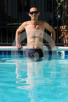 Asian man standing in swimming pool with arms on side