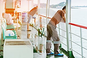 Asian man stands on baluster of ferry for relaxing and look at the ocean