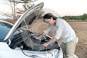 Asian man is stressed with the problem car and try to fix it by himself in the large field forest behind