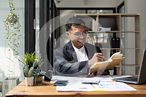 Asian man in suit using laptop and taking note writing working for business accounting finance.