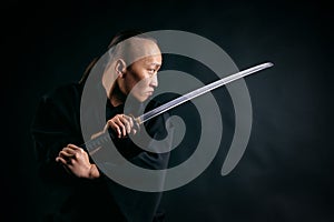 Asian man with a sword in his hands in a black robe against a black background