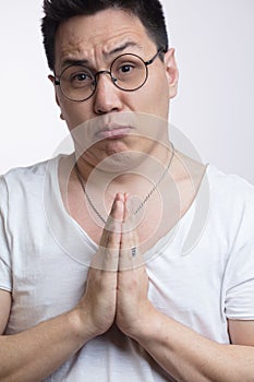 Asian man in t-shirt, holding hands in pray, begging for help or asking apology