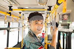 Asian man taking public transport, standing inside bus.