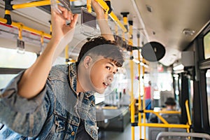 Asian man taking public transport, standing inside bus.