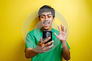 Asian man taking selfie photo or doing a video call at home, smiling to camera and waving