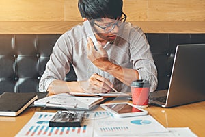 Asian man talking on his Phone and using laptop computer working on new project idea in cafe