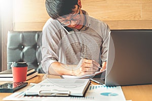 Asian man talking on his Phone and using laptop computer working on new project idea in cafe