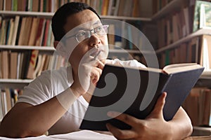 Asian man thinking while reading book, education concept, learning studying in library