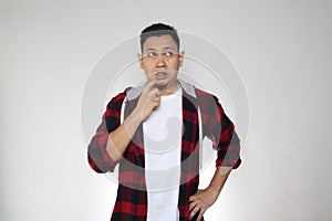 Asian man touching his lip with pointing finger, looking up and thinking hard, trying to remember gesture photo
