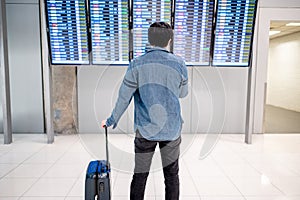 Asian man tourist at arrival departure board in airport