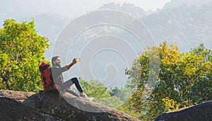 Asian man traveler using mobile phone taking selfie while solo travel on top mountain