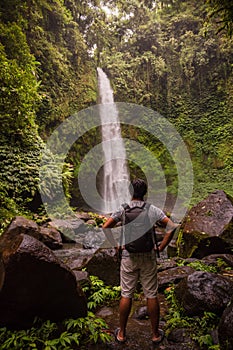 Asian man traveller enjoying waterfall landscape in tropical forest. Man with backpack. Energy of water. Travel lifestyle. View