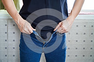 Asian man trying to button up his pants. Man's hands. Close-up. Tighten