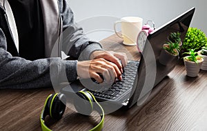 An Asian man uses a laptop at home while sitting at a wooden table