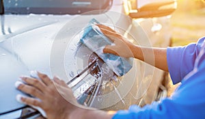 Asian man using blue sponge with soap to washing the car at outdoor in sunset time