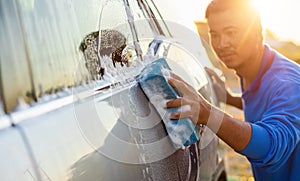 Asian man using blue sponge with soap to washing the car at outdoor in sunset time