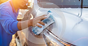 Asian man using blue sponge with soap to washing the car at outdoor in sunset time