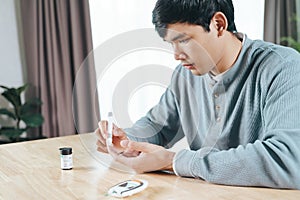 Asian man using lancet on finger for checking blood sugar level by Glucose meter, Healthcare and Medical, diabetes, glycemia