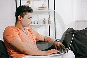 Asian man using laptop while sitting on couch at home