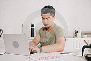 Asian man using laptop while sitting at kitchen table