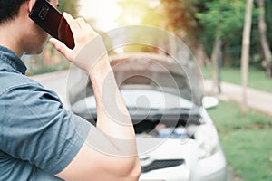 Asian man using mobile phone calling for assistance after a car breakdown on street. Concept of vehicle engine problem or accident