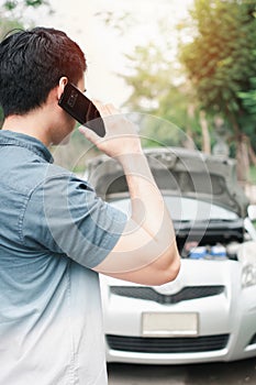 Asian man using mobile phone calling for assistance after a car breakdown on street. Concept of vehicle engine problem or accident