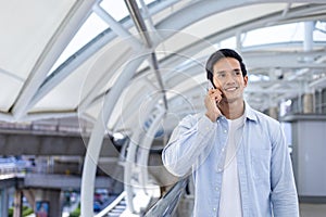 Asian man using mobile phone while walking along the urban metropolitan walk way in city downtown with copy space