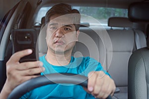 Asian man using mobile smart phone and reading messages while driving a car. Concept of negligence, dangerous behavior and