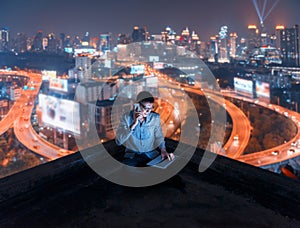 Asian man using phone and laptop with city background, technolo