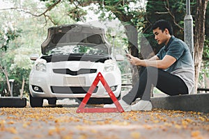 Asian man using smartphone for assistance after a car breakdown on street. Concept of vehicle engine problem or accident and