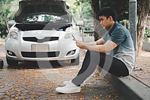 Asian man using smartphone for assistance after a car breakdown on street. Concept of vehicle engine problem or accident and