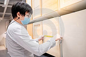 Asian man using tape measure on cabinet material