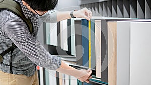 Asian man using tape measure on cabinet materials