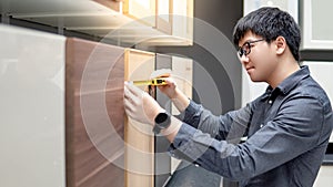 Asian man using tape measure on cabinet materials