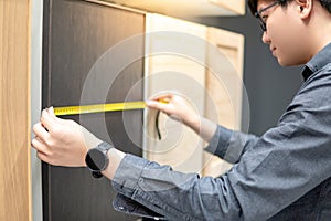 Asian man using tape measure on cabinet materials