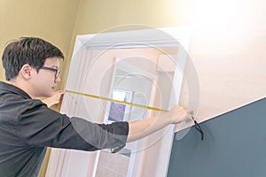 Asian man using tape measure on door frame