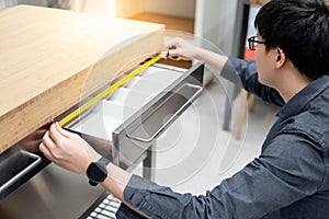 Asian man using tape measure on drawer