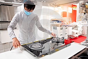 Asian man using tape measure on gas stove